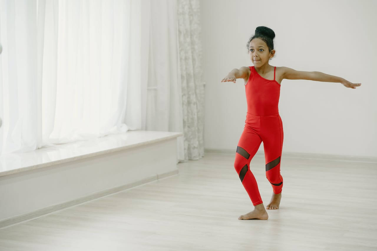A child practicing dance and wearing a red outfit. 