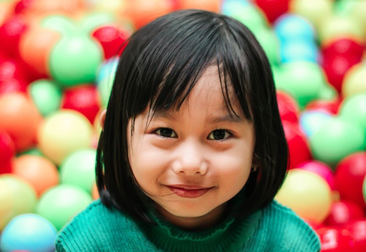 Girl smiling in ball pit at preschool gymnastics